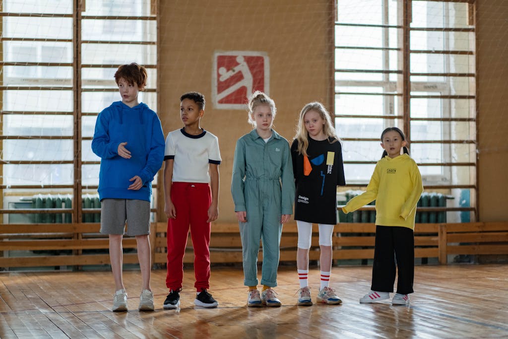A diverse group of children in a sports hall preparing for an activity, showcasing teamwork and joy.